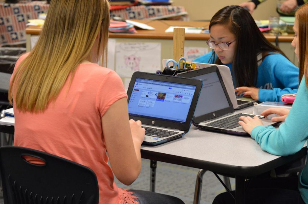 Three students working on laptops at a table in a classroom.