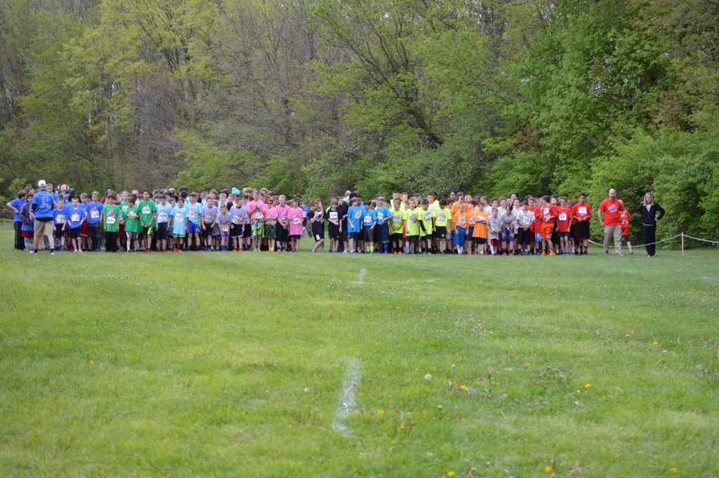 Group of people standing in a field, lined up for an event, wearing colorful shirts and hats.