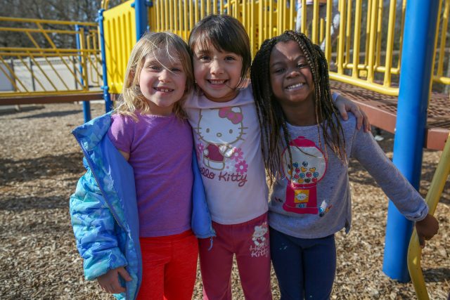three kindergarten girls on a playground smiling