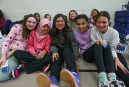 Group of young girls sitting on floor in school gymnasium, posing for picture.