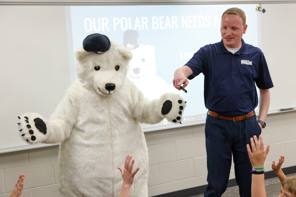 Man in blue shirt standing next to a large white teddy bear costume.