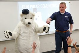 Man in blue shirt standing next to a large white teddy bear costume.