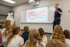A man standing in front of a classroom projector screen, gesturing while presenting to an audience.