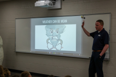 Man in front of a whiteboard explaining weather to children.
