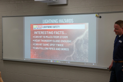 A man standing in front of a whiteboard with a presentation about lightning hazards. He is explaining the risks associated