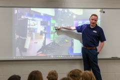 Man in front of projector screen pointing at image on screen.