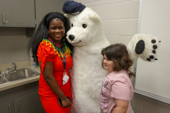 Two people posing with a large polar bear mascot in a classroom setting.