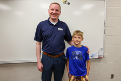 Man in blue shirt and tie standing next to a young boy.
